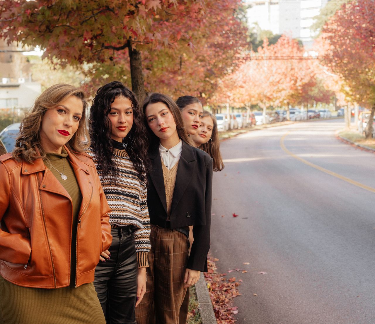 our-story-02 Group of stylish women posing on a tree-lined city street in autumn.